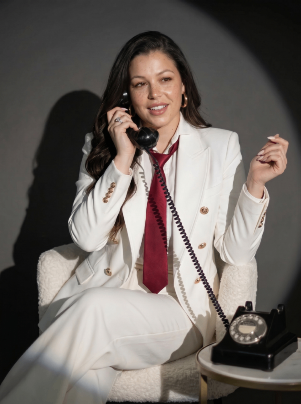 Paula seated with a vintage phone in a white suit